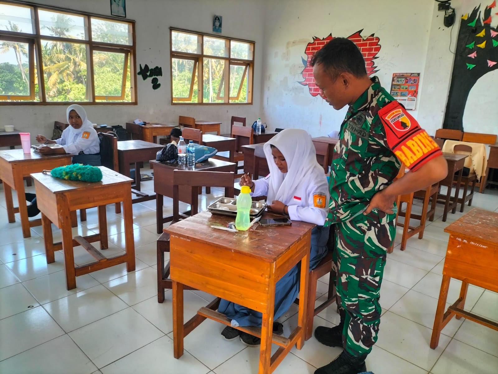 Serda Moh. Hisyam Rosadi Babinsa Kelurahan Kebalenan Kawal Distribusi Makan Siang Gratis untuk Ribuan Pelajar